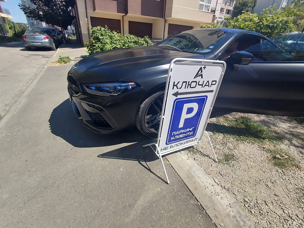 BMW M8 с матово черно покритие, паркиран пред сервизна табела А+ Ключар
